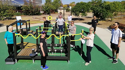 Senior citizens gathered around outdoor gym equipment