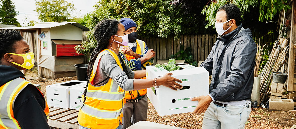 Group of volunteers, wearing masks and high visibility vests handing adult man a box of vegetables