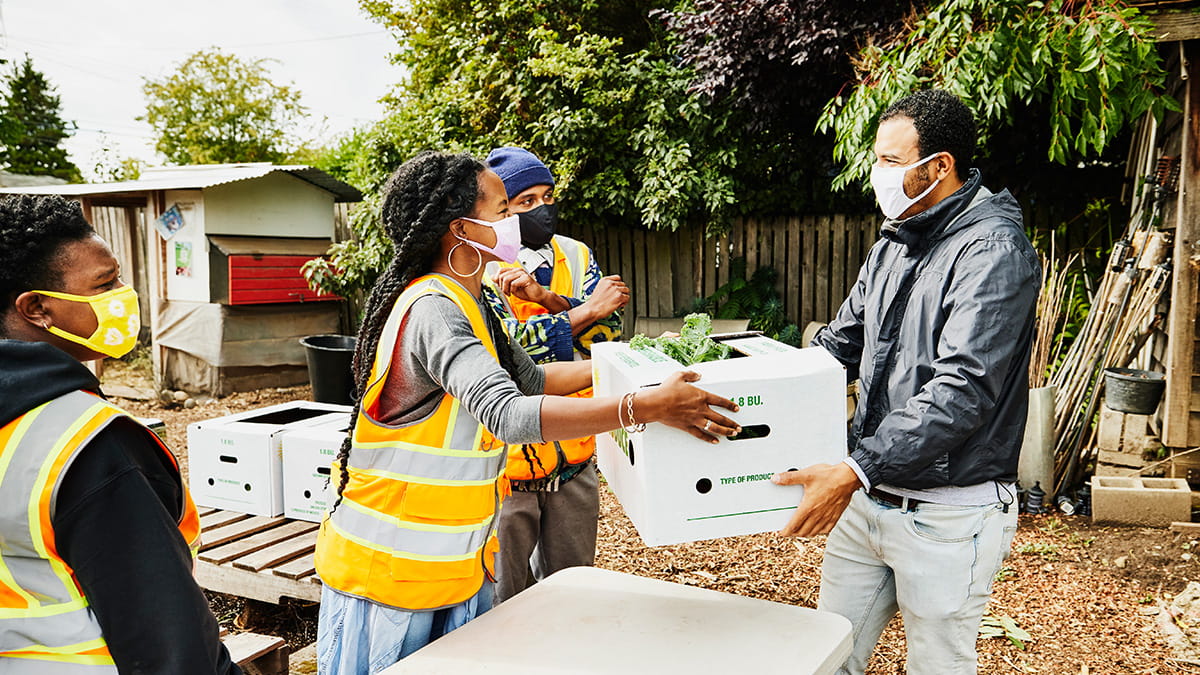 Group of volunteers, wearing masks and high visibility vests handing adult man a box of vegetables