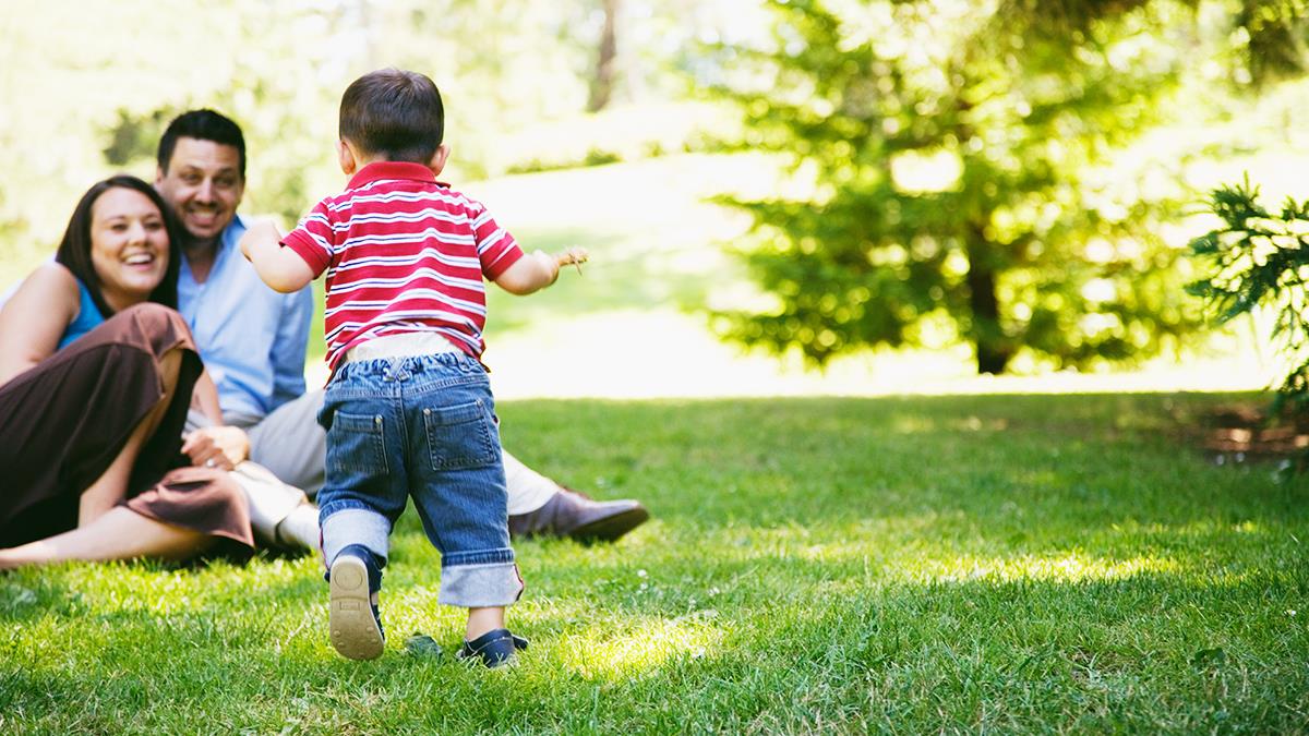 Young child walking towards parents in a park