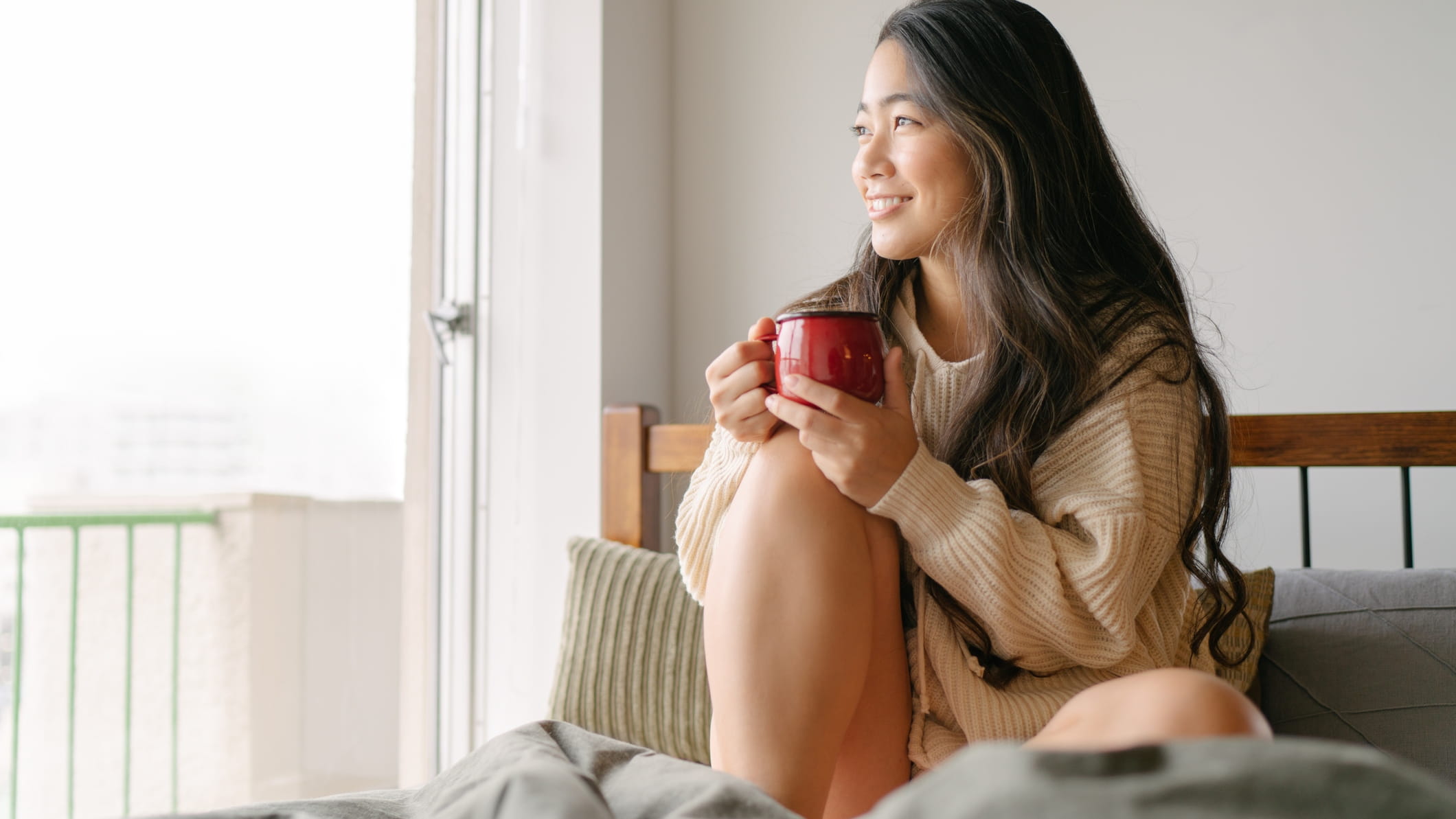 Girl sitting in bed drinking and smiling 