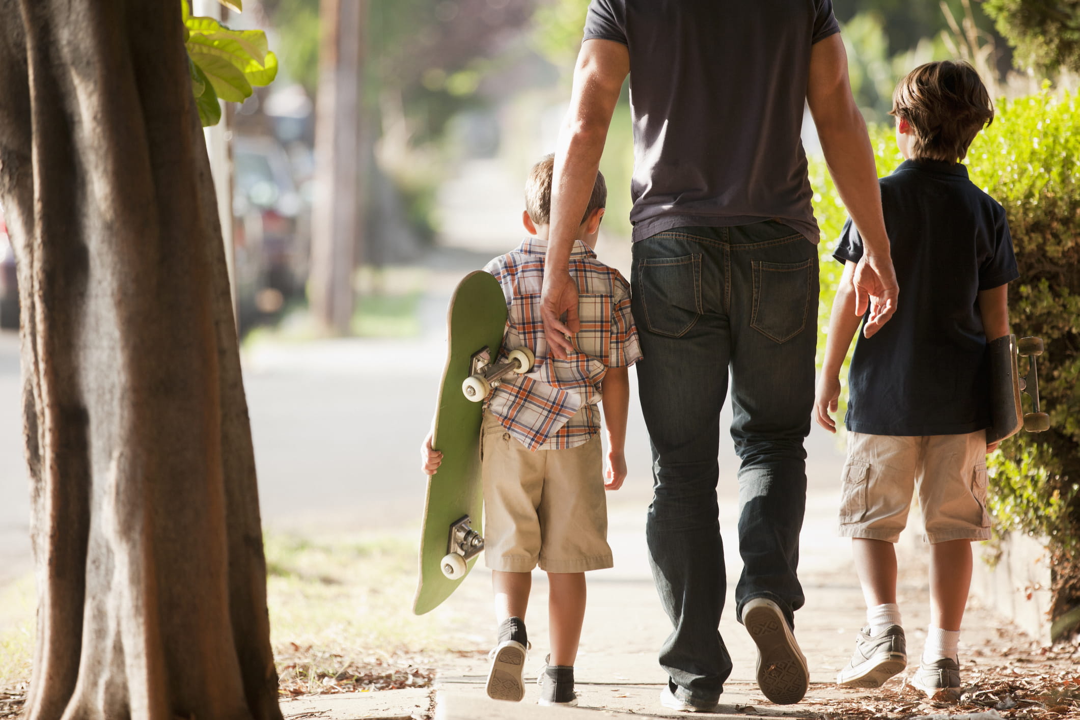 father and sons walking outdoors with skateboards