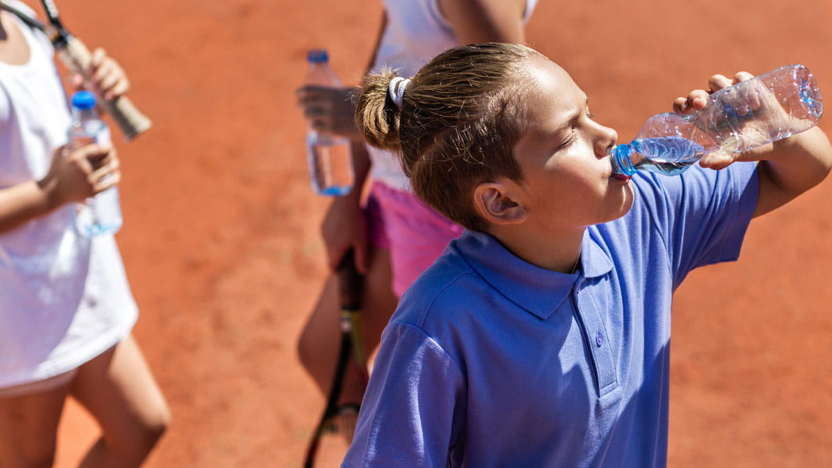 Girl with tennis racquet drinking water