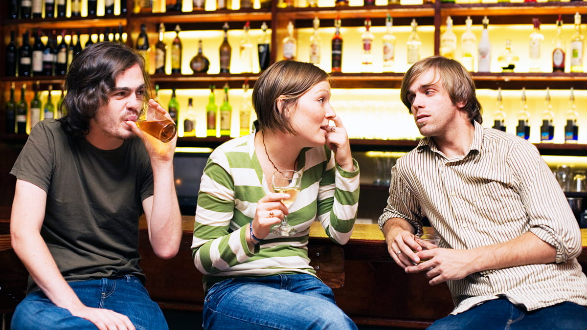 Two young men and a young woman drinking at a bar