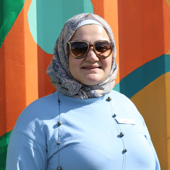 Headshot of Jude wearing a blue top, sunglasses and a hijab  