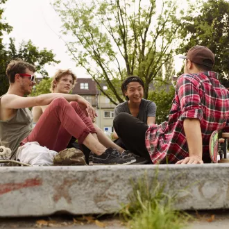 Four boys are sitting on the ground next to their skateboards.