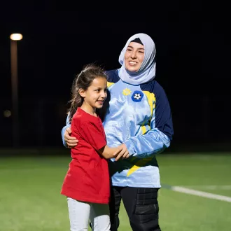 An adult (Emine) wearing a head scarf and a child on a soccer field