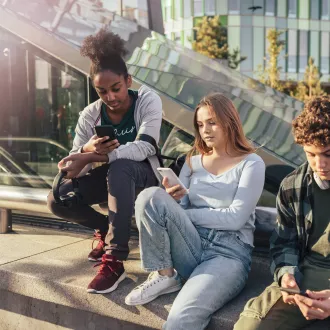 Three young people are sitting in a outdoor public area. They are all looking at their phones.