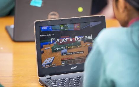 A photo looking over the shoulder of a child playing Minecraft. The text on the screen says "Players agree! Impacts 'Feeling Connected'."