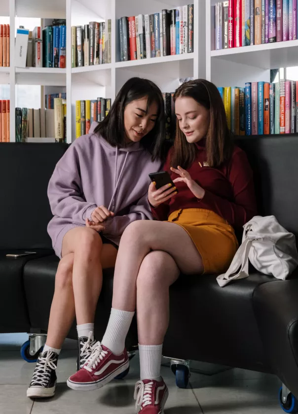 A photo of two young people in a library looking at a phone together