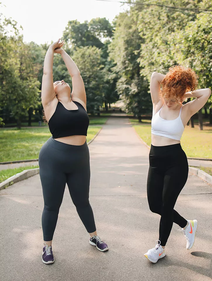 Two women outside in a park stretching and exercising.
