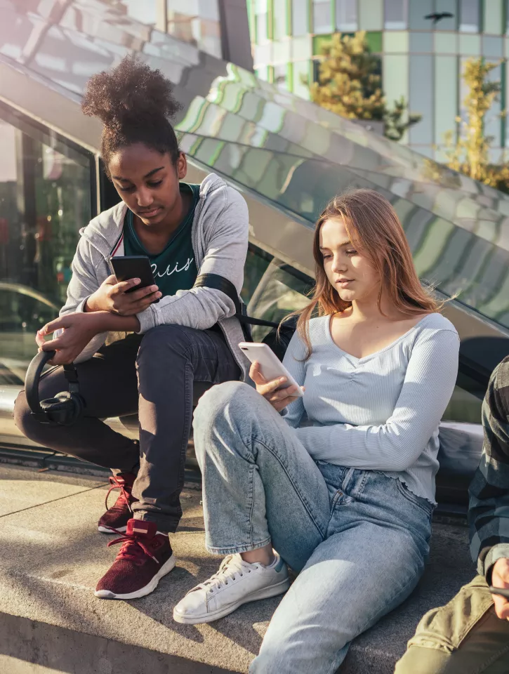 Three young people are sitting in a outdoor public area. They are all looking at their phones.